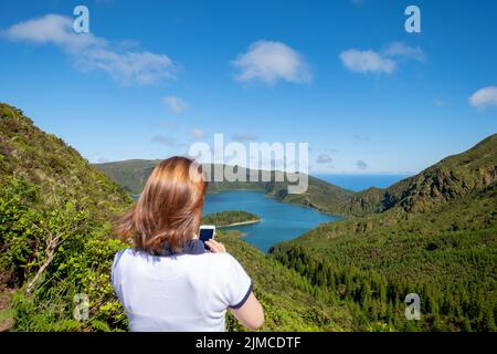 Paysage du lac de feu 'Lagoa do Fogo' dans l'île de São Miguel. Avec une femme touristique avec une vue de smartphone de derrière. Açores, Portugal, Europe. Banque D'Images