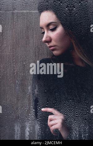 Jeune femme vue par l'humidité sur une fenêtre Banque D'Images