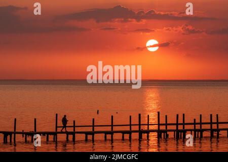 Un homme se balade le long d'un quai à Fairhope, Alabama, tandis que le soleil se couche sur Mobile Bay. Banque D'Images