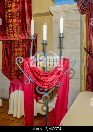 Chandelier en fer avec trois bougies allumées ornées d'un tissu rouge texturé pendant une fête. Banque D'Images