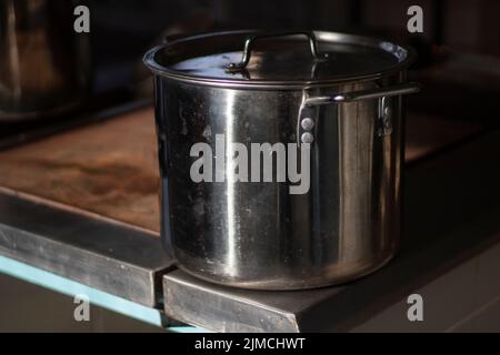 Une grande casserole est chauffée sur la cuisinière. Couverts dans la cuisine. Détails de la cuisine dans la salle à manger. Poêle en chrome aux rayons du soleil. Banque D'Images