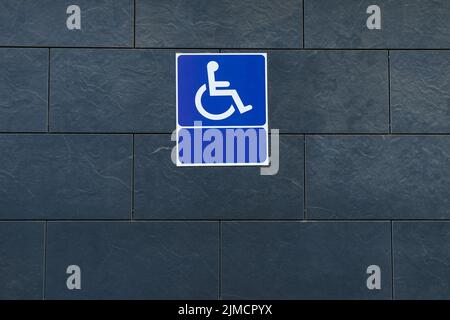 Panneau d'accessibilité bleu attaché au mur de carrelage gris foncé du bâtiment moderne sur la rue de la ville Banque D'Images