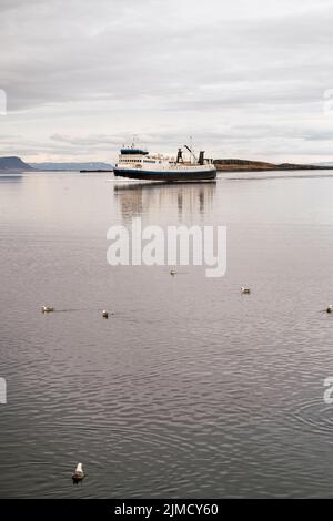 Bateau de pêche moderne flottant sur l'eau de mer avec des mouettes contre le ciel nuageux le jour terne en Islande Banque D'Images