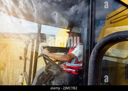 Vue latérale de la moissonneuse-batteuse sur une récolte uniforme de céréales dans un champ agricole en milieu rural Banque D'Images