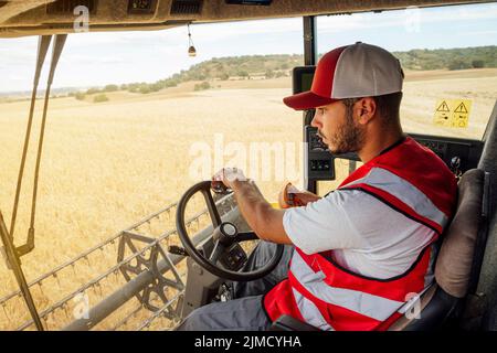 Vue latérale de l'opérateur de la moissonneuse-batteuse dans des récoltes de grains uniformes dans les champs agricoles lors de travaux en zone rurale Banque D'Images