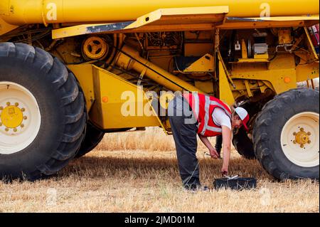 Vue latérale d'une femme joyeuse travaillant sur une moissonneuse-batteuse à l'examen uniforme dans un champ agricole à la campagne, le jour de l'été Banque D'Images