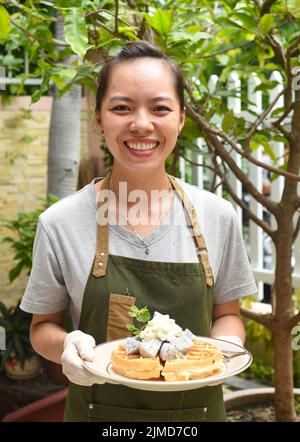 Une serveuse vietnamienne sert des gaufres belges avec des fruits et de la crème glacée dans un café extérieur Banque D'Images
