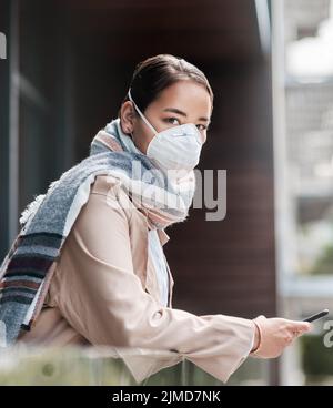 La distanciation sociale ne signifie pas l'isolement social. Une jeune femme portant un masque et utilisant un smartphone sur le balcon à la maison. Banque D'Images