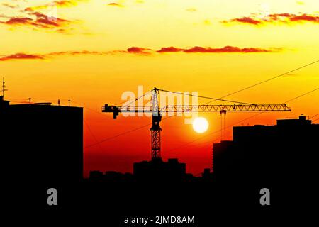 Silhouettes de maisons et grue de construction contre le soleil couchant, horizon de la ville au coucher du soleil Banque D'Images