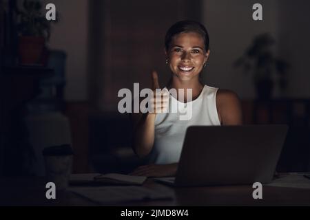 Et c'est le délai fait et dépoussiéré. Portrait d'une jeune femme d'affaires utilisant un ordinateur portable et montrant les pouces vers le haut pendant une nuit de travail. Banque D'Images