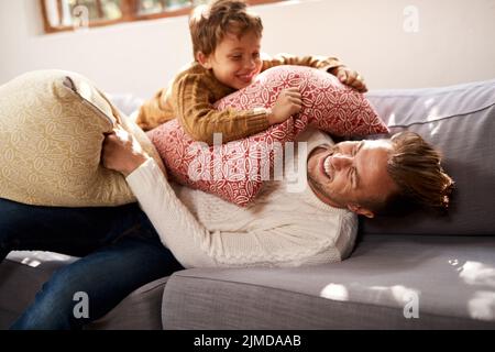 Je vous ai dit que mal vous battait. Un homme et son jeune fils ayant un combat d'oreillers sur le canapé à la maison. Banque D'Images