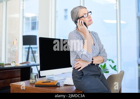 Parler traite par téléphone. Une femme d'affaires mûre parlant sur un téléphone portable dans un bureau. Banque D'Images