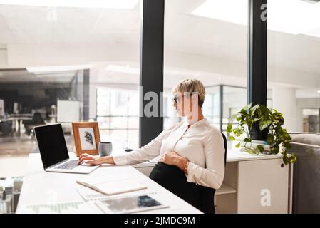 Elle prépare de grands projets pour l'avenir de son entreprise et de sa carrière. Une femme d'affaires enceinte travaillant sur un ordinateur portable dans un bureau. Banque D'Images