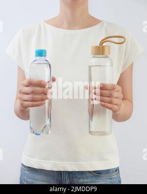 Deux bouteilles de verre et de plastique d'eau propre dans les mains d'une femme. Banque D'Images