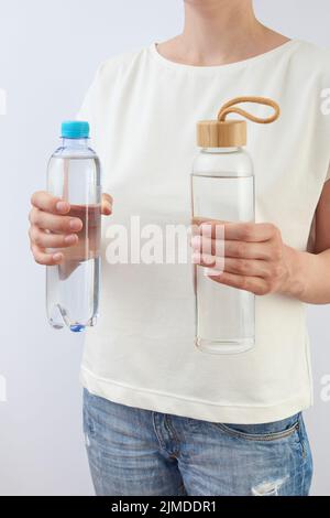 La femme tient deux bouteilles de verre et de plastique d'eau douce propre. Banque D'Images