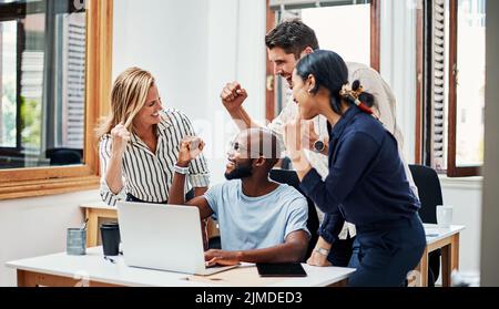 C'est ce que nous avons fait. Un groupe de collègues qui applaudissent tout en se réunissant autour d'un ordinateur portable au bureau. Banque D'Images