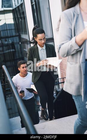 Une jeune femme d'affaires se tourne vers le succès en regardant son ordinateur portable tout en marchant dans les escaliers dans un lieu de travail moderne. Banque D'Images