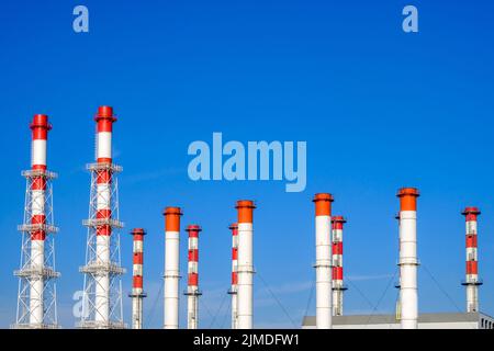 Tuyaux industriels blancs et rouges contre un ciel bleu sans nuages. Banque D'Images