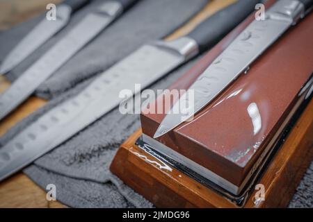 Attention sélective sur la lame d'un couteau de cuisine en acier couché sur une pierre à affûter d'eau Banque D'Images