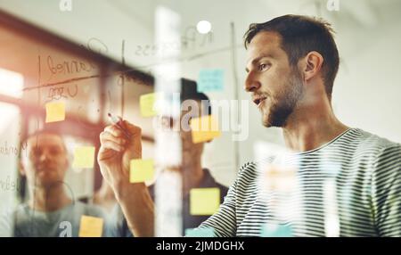 Équipe confiante, intelligente et créative qui conçoit une idée de stratégie et écrit des notes adhésives sur une planche en verre transparent. Groupe utilisant le travail d'équipe, la planification Banque D'Images