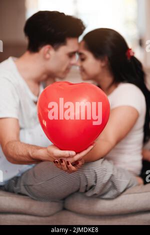 Le jour de la Saint-Valentin a été bien fait. Un jeune couple méconnaissable s'embrasse tout en tenant une montgolfière en forme de cœur le jour de la Saint-Valentin. Banque D'Images