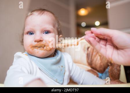 Bonne mère nourrissant sa petite fille mignonne purée de fruits de cuillère à la maison. Première nourriture Banque D'Images