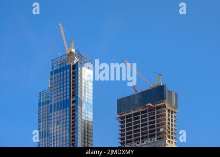 Grues de tour au sommet d'un gratte-ciel non fini contre un ciel bleu clair Banque D'Images