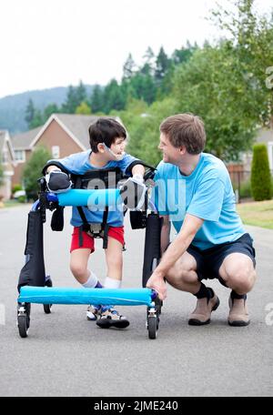 Père à genoux à côté de fils handicapé debout dans Walker Banque D'Images