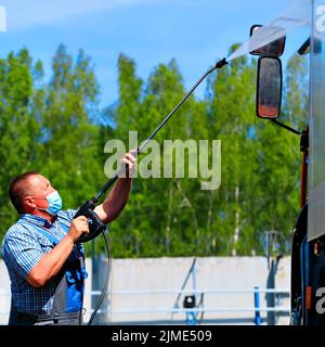 Lavage de voiture pour équipement spécial et camions. Un conducteur de sexe masculin portant un masque médical lave un camion Banque D'Images