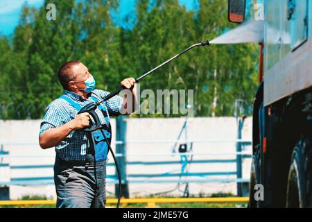 Lavage de voiture pour équipement spécial et camions. Un conducteur de sexe masculin portant un masque médical lave un camion Banque D'Images