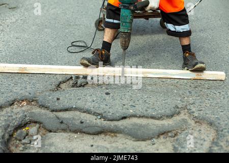 Il enlève l'asphalte avec un marteau à inertie. Retrait de la couche d'asphalte de la route. Banque D'Images