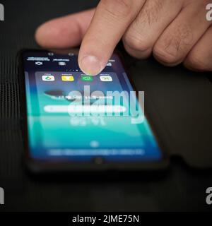 Les doigts d'une personne actionnent un smartphone allongé sur la table et sélectionnent une application Banque D'Images
