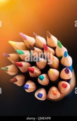 Nouveaux crayons de couleur accentuée sur un fond sombre avec lumière du soleil ou éclairage. Arrière-plan abstrait sur un thème créatif. Banque D'Images