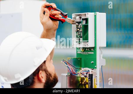 Un ingénieur électricien qualifié installe un dispositif de contrôle et de mesure dans une installation industrielle le jour de l'été. Banque D'Images