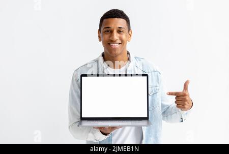 Jeune Afro-américain avec ordinateur portable sur fond blanc Homme pointe son doigt sur l'écran blanc de l'ordinateur portable Banque D'Images