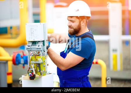 Un ingénieur électricien qualifié installe un dispositif de contrôle et de mesure dans une installation industrielle le jour de l'été. Banque D'Images