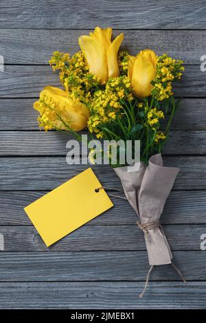 Bouquet de fleurs jaunes avec carte en papier vierge comme un étiquette pour le nom ou les salutations sur fond en bois Banque D'Images