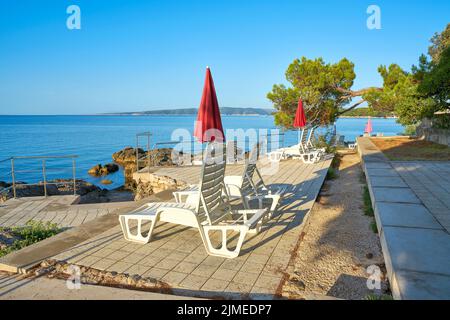 Parasols et chaises longues sur un lieu de baignade typique sur la côte de la ville de Krk Banque D'Images