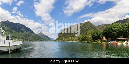 Super vue panoramique sur le lac glaciaire Idro (Lago d'Idro), de nombreux bateaux de pêche sèchent sur l'herbe verte du rivage, en premier plan un passager Banque D'Images