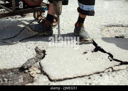 Il enlève l'asphalte avec un marteau à inertie. Retrait de la couche d'asphalte de la route. Banque D'Images