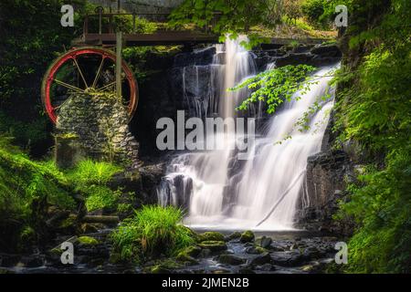 Roue d'eau rouge vintage avec chute d'eau au printemps dans le parc forestier de Glenariff, en Irlande du Nord Banque D'Images