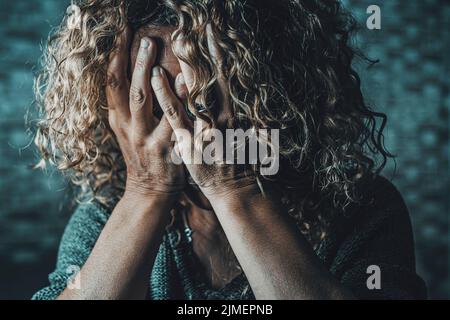 Gros plan d'une femme désespérée avec les mains sur le visage dans l'obscurité à la maison. Situation de la criminalité liée à la violence sexuelle dans la famille. Pleurs femelles stressées et effrayées. Lonelin Banque D'Images