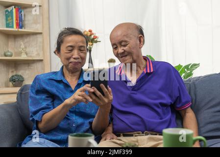 Des personnes âgées asiatiques utilisant la technologie de communication Internet en ligne de téléphone mobile à la maison. Banque D'Images