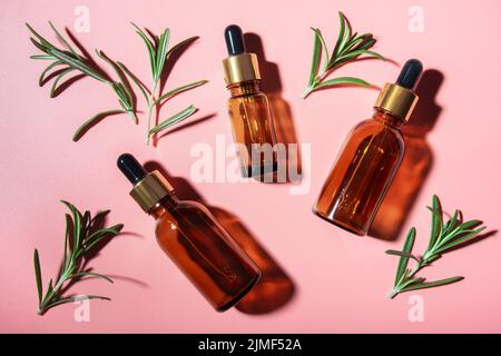 Flacons compte-gouttes avec feuilles d'huile et de romarin sur table rose, vue sur la pose.Concept de cosmétiques à base de plantes Banque D'Images