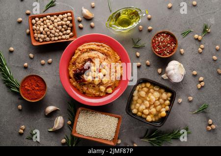 Houmous recouvert de pois chiches, huile d'olive et tomate séchée au soleil sur table en pierre avec différentes épices de côté. Pose plate Banque D'Images