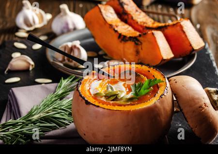 Coque de citrouille avec soupe de citrouille rustique maison avec des graines sur plateau d'ardoise avec des épices de côté Banque D'Images