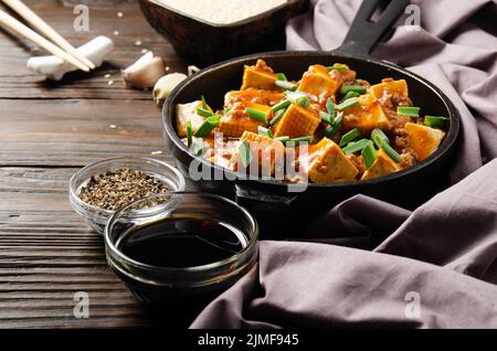 Mapo tofu dans une poêle en fonte avec ciboulette hachée de porc sauce soja poivre du sichuan ail et épices à proximité sur une table en bois Banque D'Images