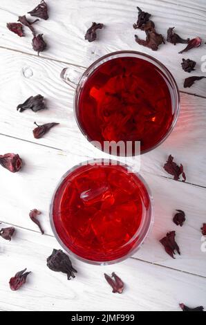 Vue supérieure à deux tasses de thé avec de la glace sèche et pétales d'hibiscus sur fond de table en bois blanc Banque D'Images