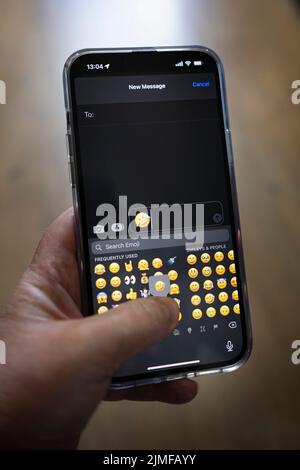 IPhone 13 pro max étant tenu avec une main caucasienne textant une pleurs avec le rire emoji Banque D'Images