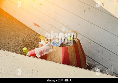 Coucher de soleil, sac en papier avec ordures en plastique et ordures éparpillées. Banque D'Images